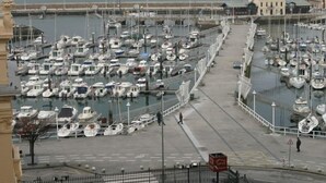 A marina with numerous boats docked in rows, a pedestrian walkway, and a view of the sea and distant buildings. - Hotel Don Manuel (Gijon)