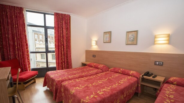 A hotel room with two beds, a desk, a chair, and a window with curtains.