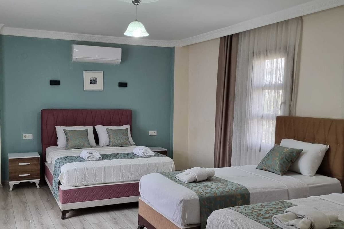 Een hotelkamer met twee bedden, een plafondventilator, een airconditioning en een raam met gordijnen.