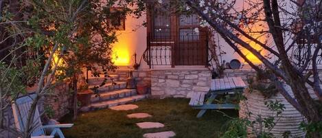 A stone staircase leading to a wooden door, surrounded by a grassy area with stepping stones and a chair.