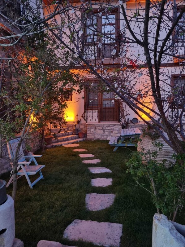 A stone staircase leading to a wooden door, surrounded by a grassy area with stepping stones and a chair. - Sezgin Boutique Hotel (Kusadasi)