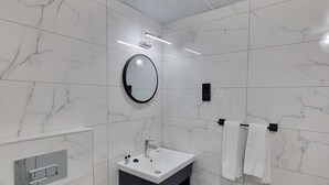 Un baño moderno con piso de mármol, espejo redondo, lavamanos blanco y retrete.