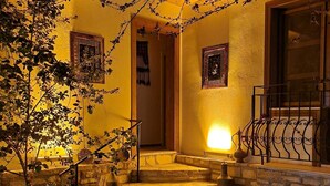 Un espacio exterior bien iluminado con escalones de piedra que conducen a una puerta, rodeado de plantas en macetas y un pequeño jardín con piedras para pisar.