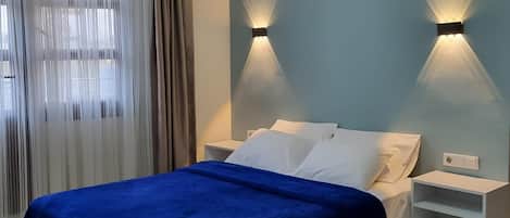 A bedroom with a bed, two bedside tables, an air conditioning unit, and a ceiling light fixture.