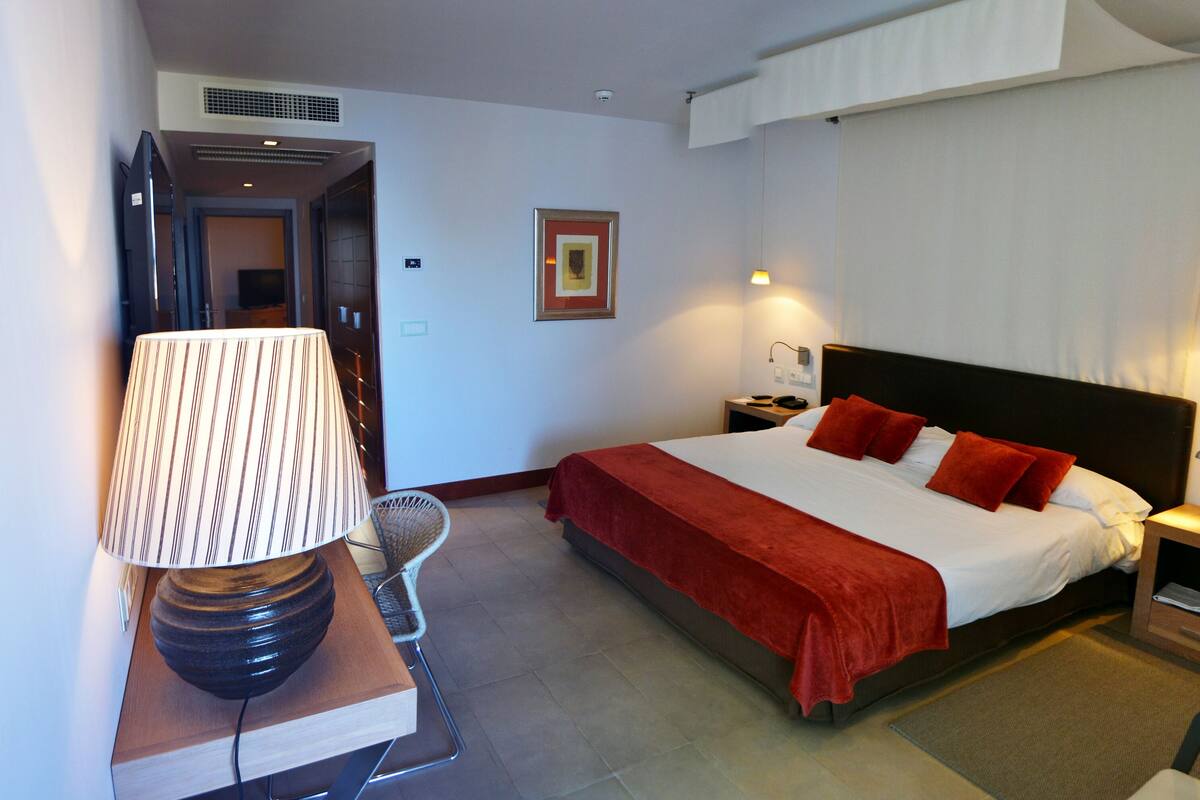 Une chambre d’hôtel avec un lit, des tables de chevet, une lampe, une chaise et une petite table sur laquelle se trouve un magazine.