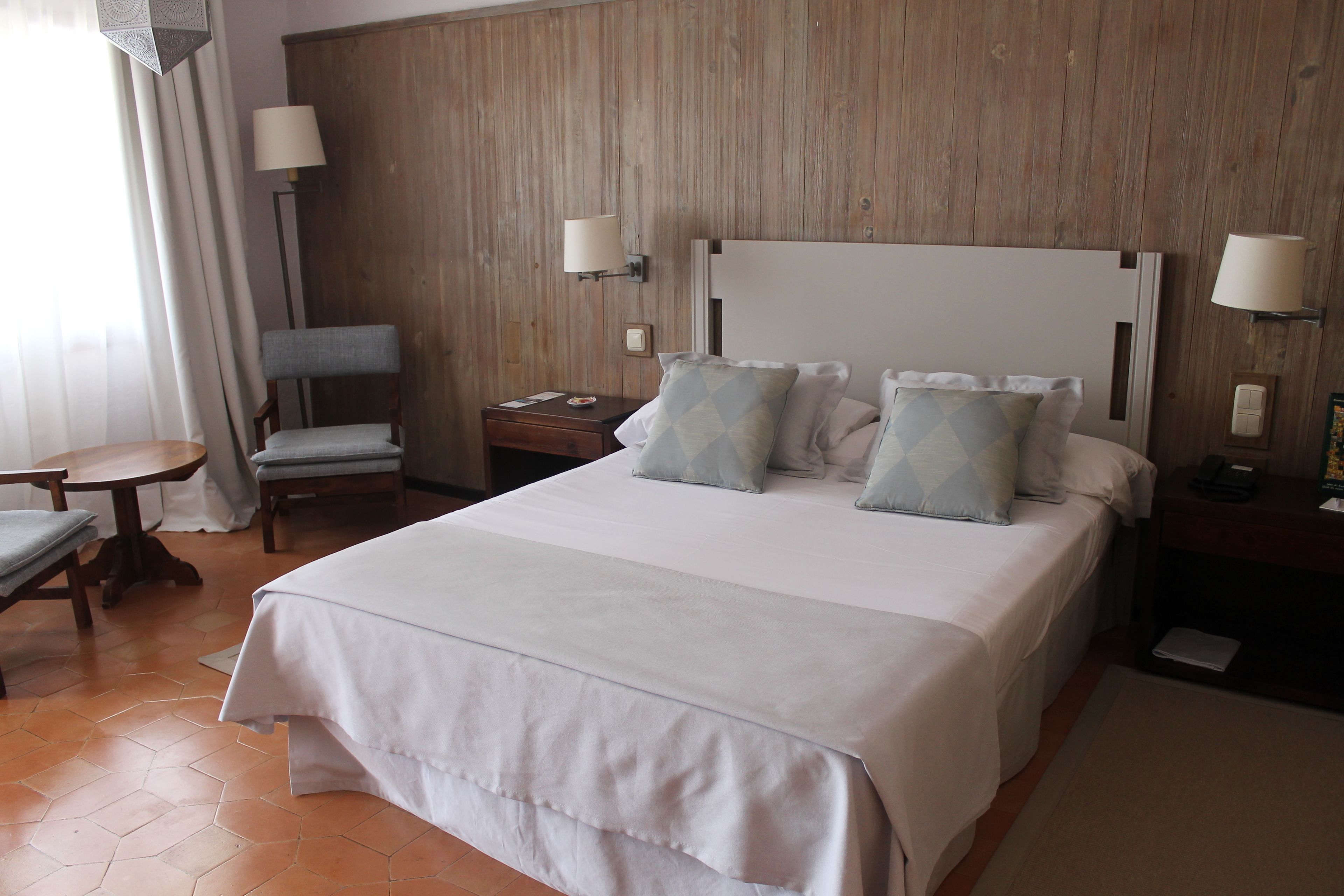 A hotel room with a large bed, two bedside tables, a chair, and a lamp.