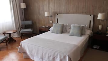 Una habitación de hotel con una cama grande, dos mesitas de noche, una silla y una lámpara.