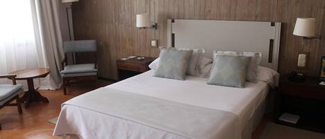 Una habitación de hotel con una cama grande, dos mesitas de noche, una silla y una lámpara.