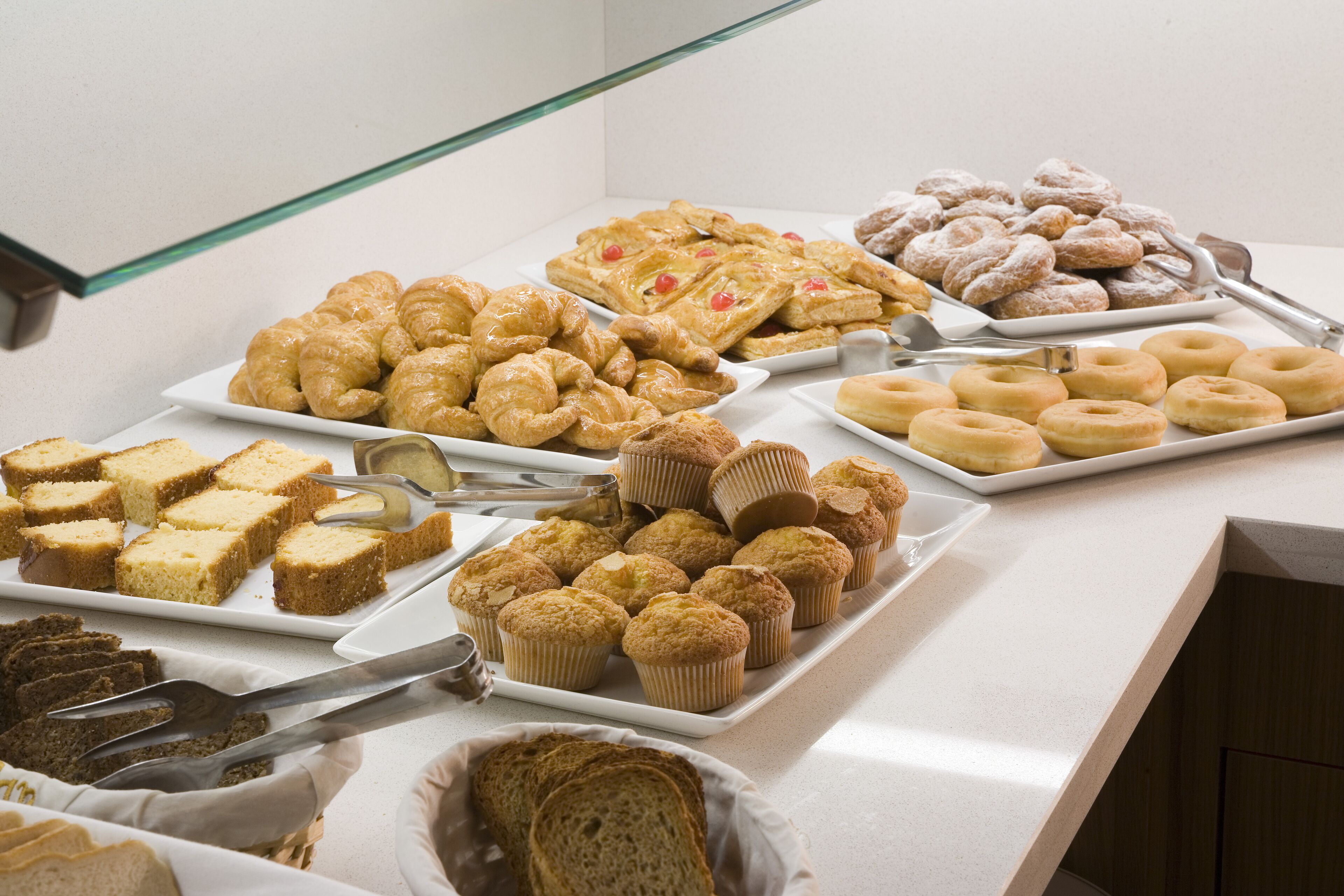 A buffet with various baked goods including pastries, muffins, and donuts.
