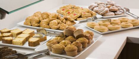 A buffet with various baked goods including pastries, muffins, and donuts.