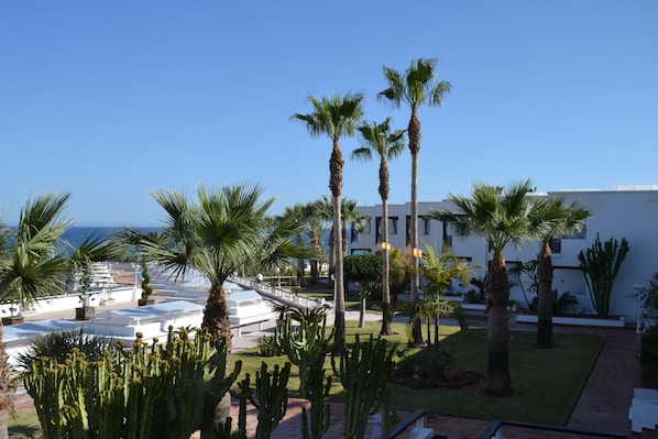 A hotel courtyard with palm trees, a pool area, and a view of the ocean. - Parador de Mojácar (Mojacar)