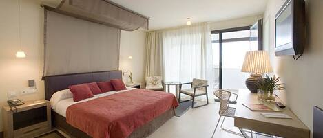 Habitación de hotel con cama, mesitas de noche, escritorio, silla, lámpara y televisión.