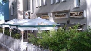 A building with a sign reading "RESTAURANT" and "Semenstadt". There are outdoor umbrellas and a fence in front.