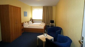 A hotel room with a bed, a desk with a chair, a TV, and a wardrobe.