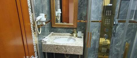 A bathroom with a marble sink, a large mirror with a gold frame, a shower enclosure, and a patterned floor.