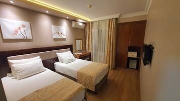 Ein Hotelzimmer mit zwei Betten, einem Holzkopfteil, einem Nachttisch mit Lampe, einem Spiegel und einem Kleiderschrank.