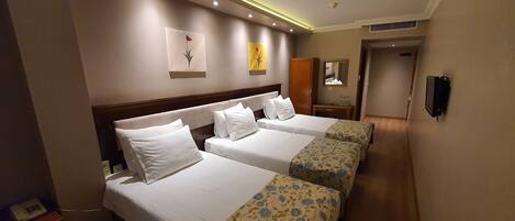 A hotel room with two beds, a wooden headboard, a bedside table with a lamp, a mirror, and a wall-mounted phone.