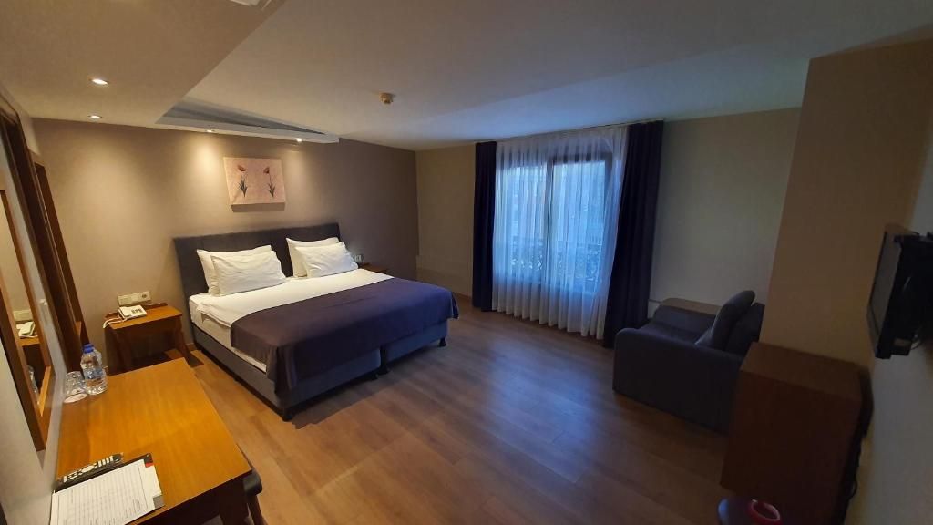 A hotel room with a bed, a desk, a chair, and a large window with curtains.