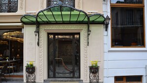 Entrada de hotel con intrincados detalles de hierro forjado, un toldo verde y un felpudo.