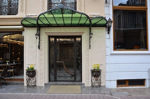A hotel entrance with ornate ironwork, a green awning, and a doormat.