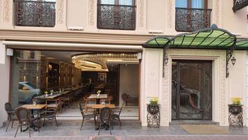 Exterior de un hotel con zona de comedor, barandillas de hierro ornamentadas y toldo verde.
