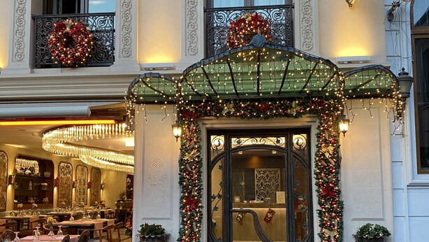 Entrada de hotel con fachada decorada, un candelabro y un área de comedor visible en el interior.