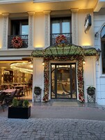 A hotel entrance with a decorated facade, a chandelier, and a dining area visible inside.