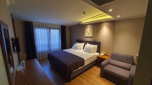 Una habitación de hotel con una cama, una silla, una mesita de noche con teléfono y una ventana con cortinas.