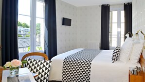 A hotel room with a bed, a chair, a table with a vase of flowers, and a window with curtains. - Hôtel du Manoir (Tours)