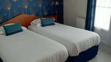 Habitación de hotel con dos camas, una pared azul estampada y un ventanal con cortinas.