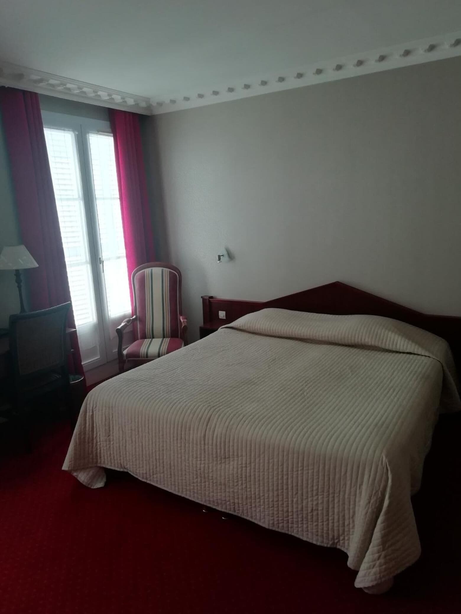 Une chambre d’hôtel avec un lit, une chaise, un bureau et une fenêtre avec des rideaux.