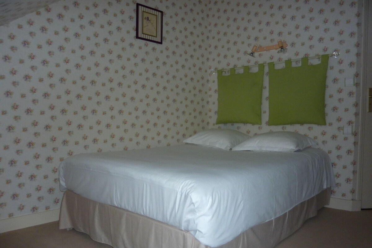 A bedroom with a bed, floral wallpaper, and a picture on the wall.