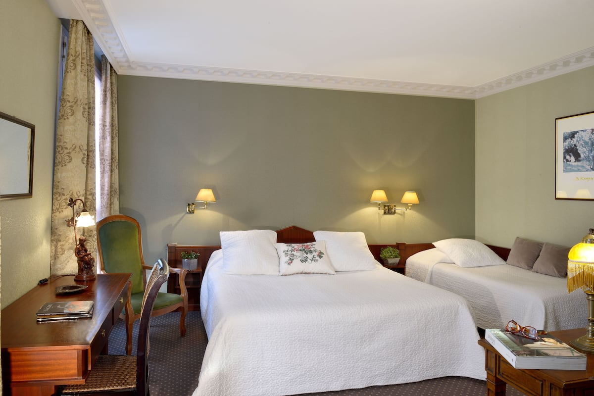 A hotel room with two beds, a desk with a chair, a lamp, and a framed picture on the wall.