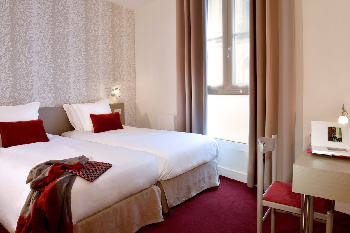 A hotel room with two beds, a desk, and a chair.