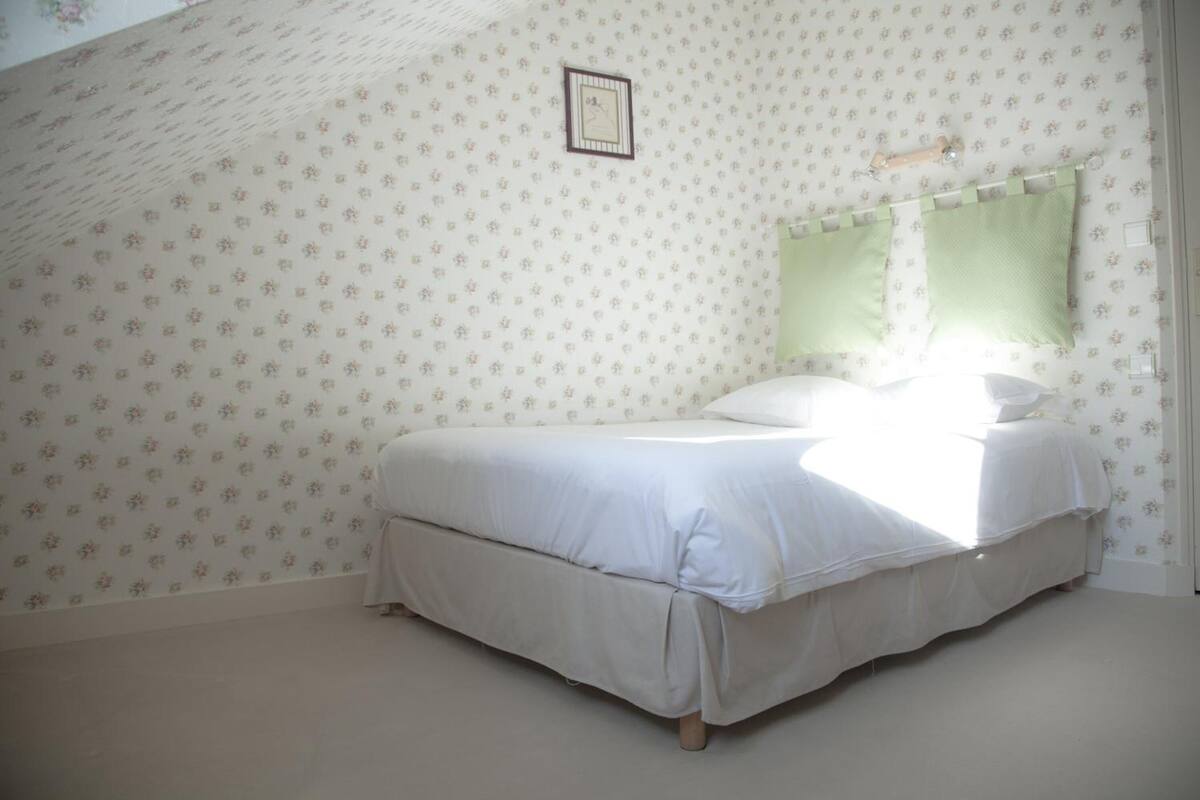 A bedroom with a bed, floral wallpaper, and a framed picture on the wall.