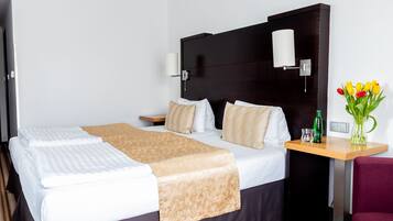 Una camera d'albergo con un letto grande, un comodino con una lampada, un tavolino con un vaso di fiori e una sedia.
