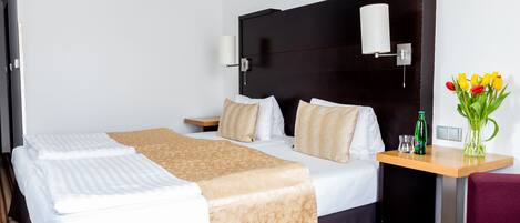 A hotel room with a large bed, a bedside table with a lamp, a small table with a vase of flowers, and a chair.