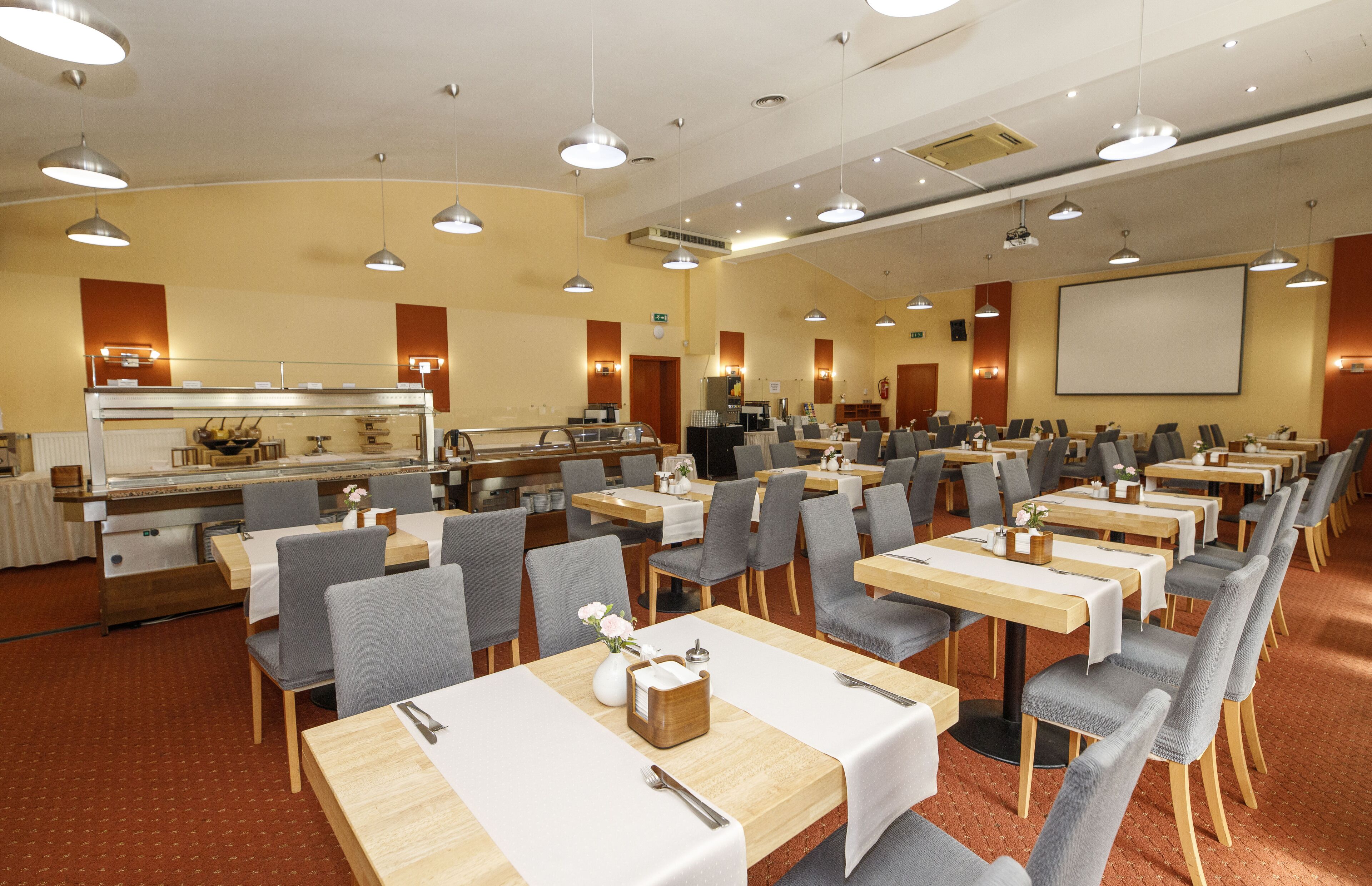 A conference room with multiple tables and chairs, a buffet area, and a projection screen.