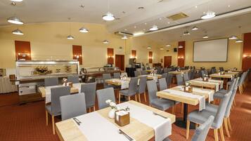 A conference room with multiple tables and chairs, a buffet area, and a projection screen.