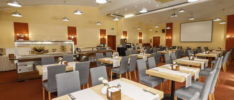A conference room with multiple tables and chairs, a buffet area, and a projection screen.