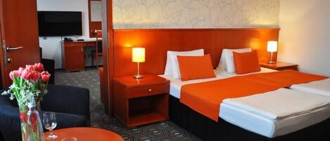 A hotel room with a large bed, two bedside tables with lamps, a desk with a chair, a TV, and a vase with flowers.