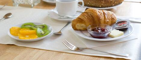 Desayuno con croissants, gajos de naranja, kiwi, mermelada y un paquete de Nutella sobre un plato blanco.