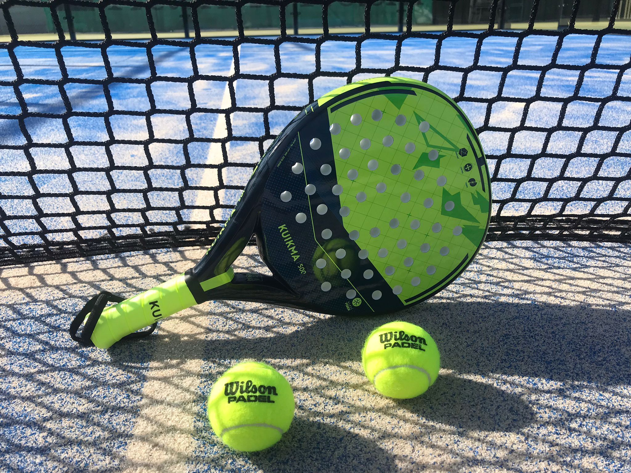 A tennis racket and two tennis balls on a court with a net.