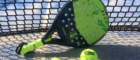 A tennis racket and two tennis balls on a court with a net.