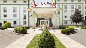 Entrada de hotel con un toldo central, varias banderas y un jardín bien cuidado.