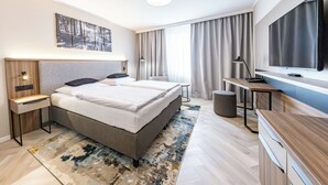 Una habitación de hotel moderna con una cama grande, un escritorio, un televisor y un cuadro en la pared.