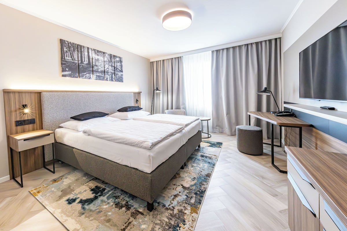Une chambre d’hôtel moderne avec un grand lit, un bureau, une télévision et un tableau au mur.