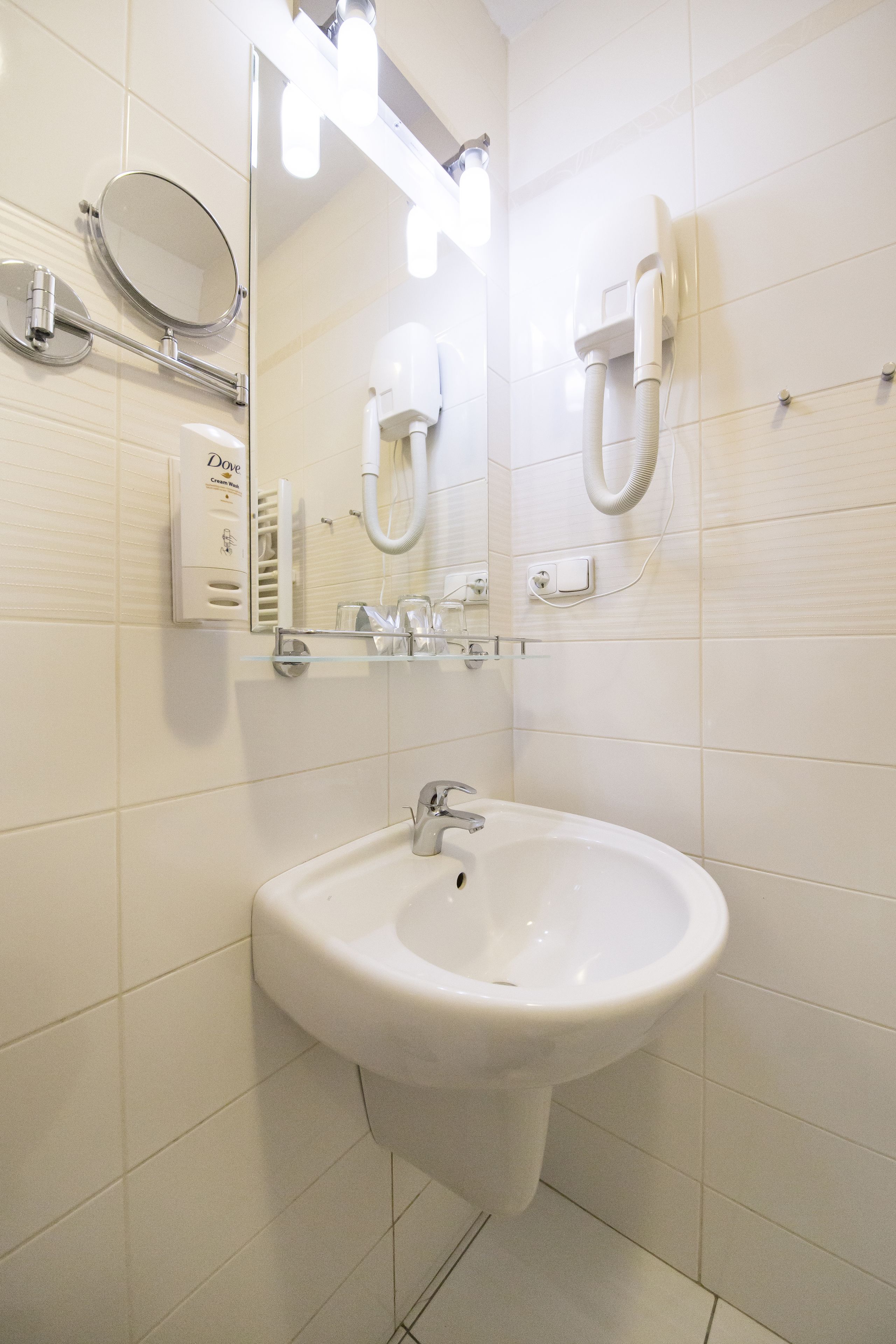 Un baño con un lavamanos blanco, un espejo y un secador de pelo en la pared.