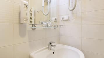 Un baño con un lavamanos blanco, un espejo y un secador de pelo en la pared.
