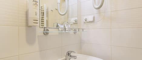 A bathroom with a white sink, a mirror, and a hairdryer on the wall.